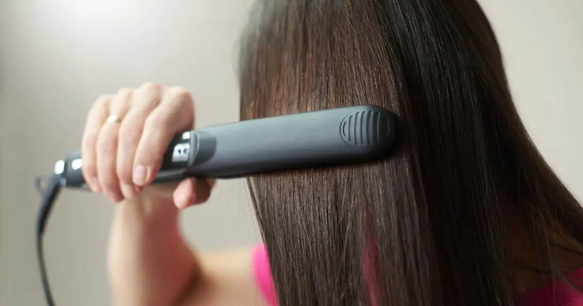 Brunette woman straightens her hair using an iron hair straightener Brunette woman straightens her hair using an iron hair straightener